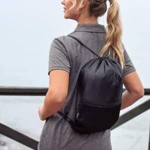 A black drawstring bag is worn on the back of a person against a scenic outdoor backdrop.
