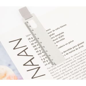 A clear ruler bookmark in light grey, positioned on a printed text page. It features a measurement scale and a branding logo.