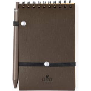 A brown spiral notebook made from coffee fibre with a pen attached by an elastic band. It features a logo.