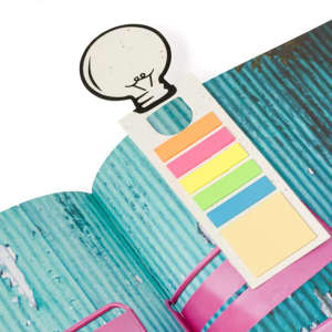 A bookmark featuring a lightbulb design and various coloured sticky notes, positioned in an open book with a blue textured background.