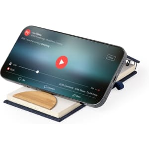 A navy Alyxa Holder Notebook with a smartphone displaying a video on top, featuring a wooden stand.