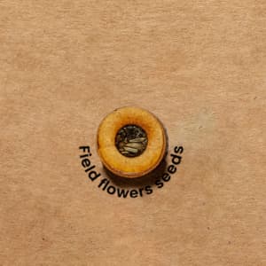 A circular seed packet with a wooden appearance, filled with field flower seeds on a brown background.