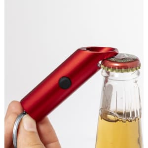 A red keyring bottle opener with a torch function is being used to open a beer bottle. It features a circular logo.