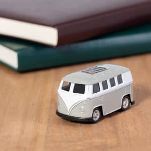 A novelty item shaped like a grey and white vintage van, placed on a wooden surface beside green and maroon notebooks.