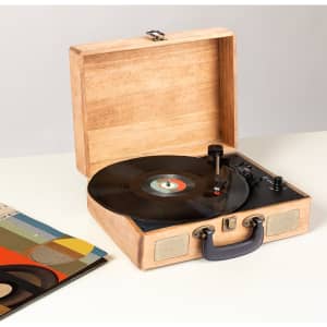 A wooden vinyl record player with a black turntable and open case, accompanied by an album cover featuring geometric designs.