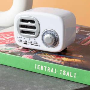 A white Florens Speaker sitting on a green book, featuring vents and a volume control dial.
