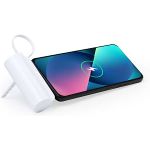 A white power bank sits next to a smartphone with a vibrant, multicoloured display featuring a charging symbol.