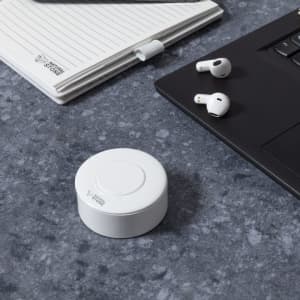 White Bekery Earphones next to a notebook and a laptop on a textured grey surface. The earphones are wireless.