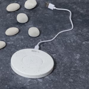 A white wireless charger with a speckled finish, accompanied by smooth pebbles on a dark surface.