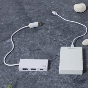 A white USB hub with multiple ports connected to a white rectangular power source on a grey stone surface.