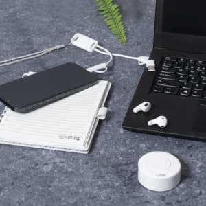 A white charging cable connected to a laptop, alongside a phone, notebook, and earbuds on a grey surface.