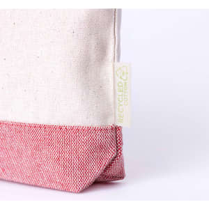 A toiletry bag with a cream canvas upper and a red patterned bottom, featuring a logo label for recycled materials.