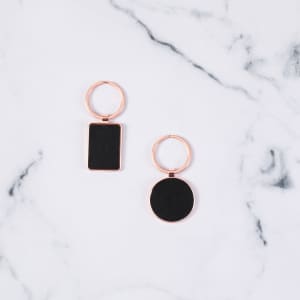 A rose gold keyring set featuring a rectangular and a circular charm on a marble background.