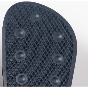 A close-up of the textured sole of navy blue flip flops with circular grips. The image features a logo.