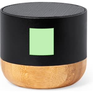 A round portable speaker with a textured black top and a wooden base, featuring a light green rectangle.