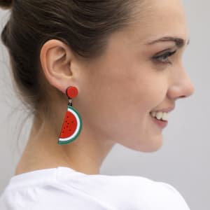 Colourful watermelon-themed earrings featuring red, green, and white accents, displayed on a model.