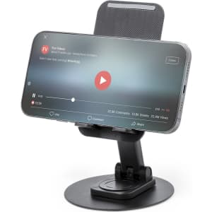 A phone stand featuring a sleek black base with a carbon fibre texture, holding a smartphone at an angle.