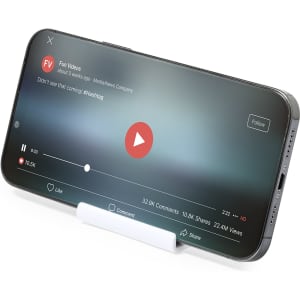 A phone stand in white holding a smartphone displaying a video playback screen, featuring a play button.