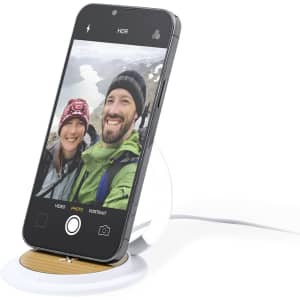 A wireless charger with a wooden base and a white stand, featuring a smartphone displaying a selfie.