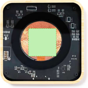 A wireless charger with a square charging pad, featuring a dark surface and intricate electronic details, set in a light wooden frame.