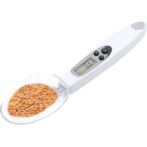A digital weighing scale in white, measuring golden seeds in a clear scoop attachment. It features a digital display and buttons.