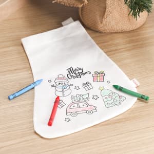 A white Christmas stocking featuring festive illustrations and three coloured crayons: red, green, and blue.