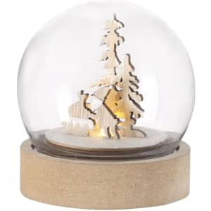 A glass snow globe featuring a wooden scene with trees and figures, set on a rustic wooden base.