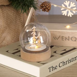 A snow globe featuring wooden trees and a deer, set on a wooden base with a warm glow.