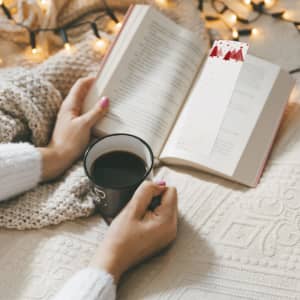 A Baird Seeds bookmark features a festive design, resting in an open book with a mug of coffee nearby.