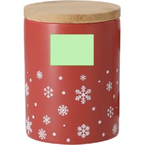A red jar with a wooden lid, featuring white snowflakes on the surface. It has a blank green label.