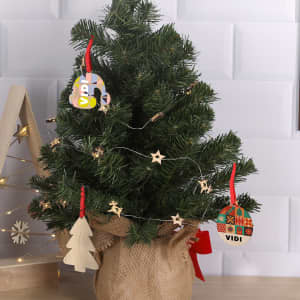 A small artificial Christmas tree decorated with wooden ornaments and a string of stars, displayed in a burlap pot.
