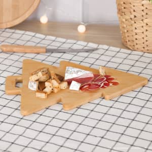 A bamboo chopping board shaped like a Christmas tree, featuring cheese and charcuterie arranged on it.