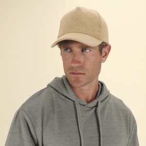 A beige cap with a ribbed texture, worn by a man in a grey hoodie. The cap features a logo on the front.