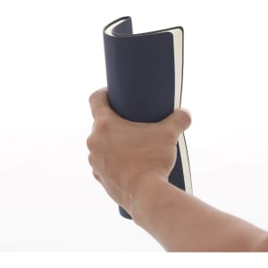 A hand holding a navy blue notepad with a cream-coloured interior, featuring a branded logo.