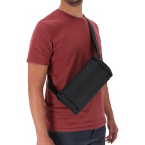 A black bag with a shoulder strap, worn by a person in a maroon t-shirt. The bag has a cylindrical shape and a logo.