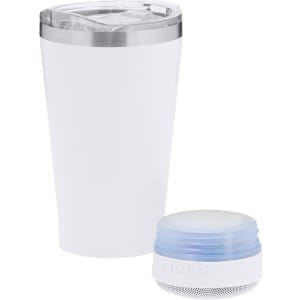A white insulated cup with a clear lid next to a round blue portable speaker. The cup has a branding logo.