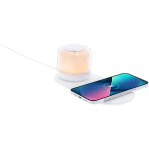 A white wireless charger lamp with a soft glowing light beside a smartphone on a charging pad.