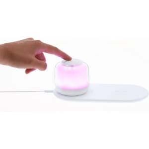 A white wireless charger lamp featuring a pink glowing dome and a hand pressing the top button.