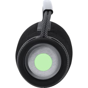 A cylindrical black speaker with a textured surface and a green light in the centre, featuring a hanging strap.