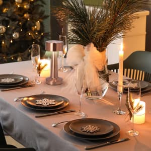 A stylish table setting featuring a silver Rosity Lamp, black plates, and festive decorations amidst a softly lit ambiance.