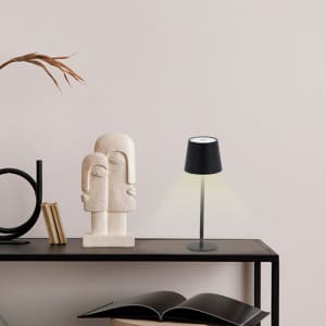 A black lamp with a round shade emits light, placed beside a stone sculpture on a modern shelf.
