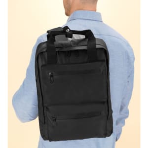 A black backpack is worn on the back of a person, featuring multiple zippered pockets and a sturdy handle.
