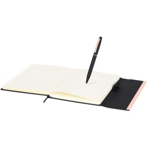 A black and pink notebook with a pen resting on an open page, featuring blank white pages. The notebook has a logo.