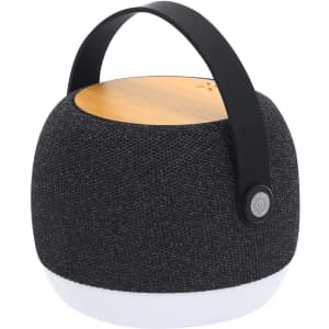 A round, black fabric-covered speaker with a wooden top and a black handle. Features a button on the side.