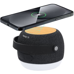 A round, grey speaker with a wooden top and a phone wirelessly charging above it. The speaker features a black strap and a logo.