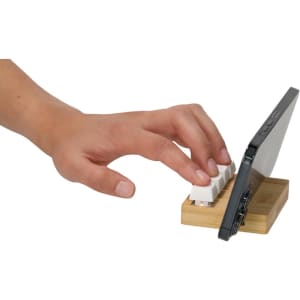 A wooden phone stand in natural colour, holding a smartphone, with a hand interacting with it.