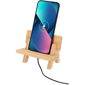 A bamboo phone stand supports a smartphone displaying a battery charging icon, with a cable connected.