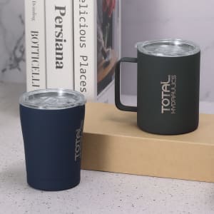 A travel mug and a cup in navy and dark green, both featuring a logo, on a neutral background with books.