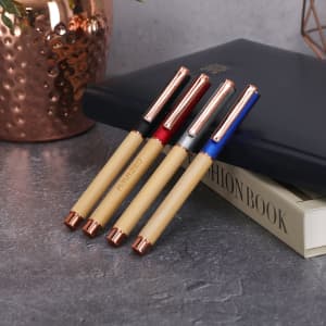Four pens with bamboo bodies and rose gold clips, featuring red, blue, and natural colours, placed on a grey surface.