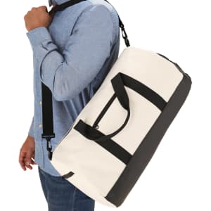 A duffle bag in white and black, featuring handles and a shoulder strap, held by a person.
